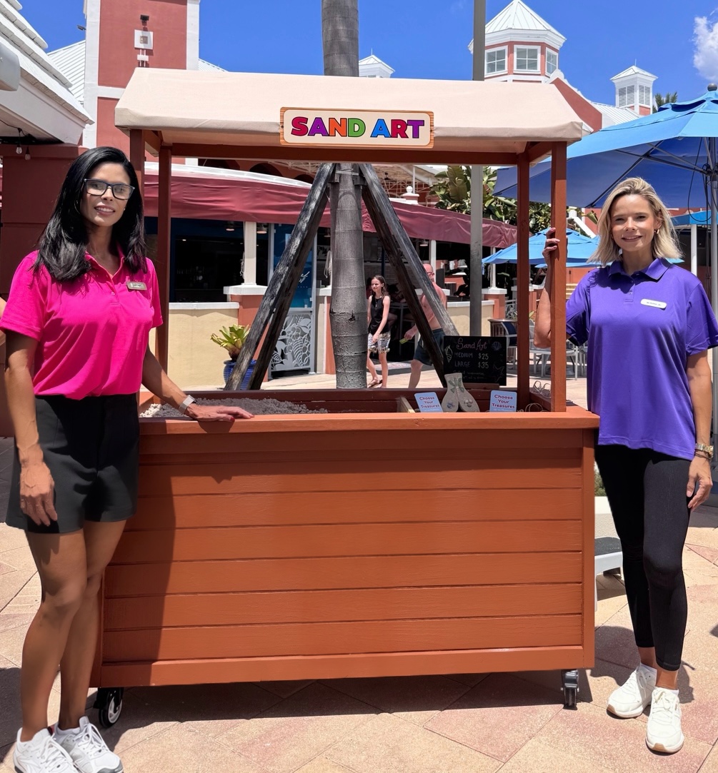 Brena's Arts & Activities sand art kiosk with team members at a resort
